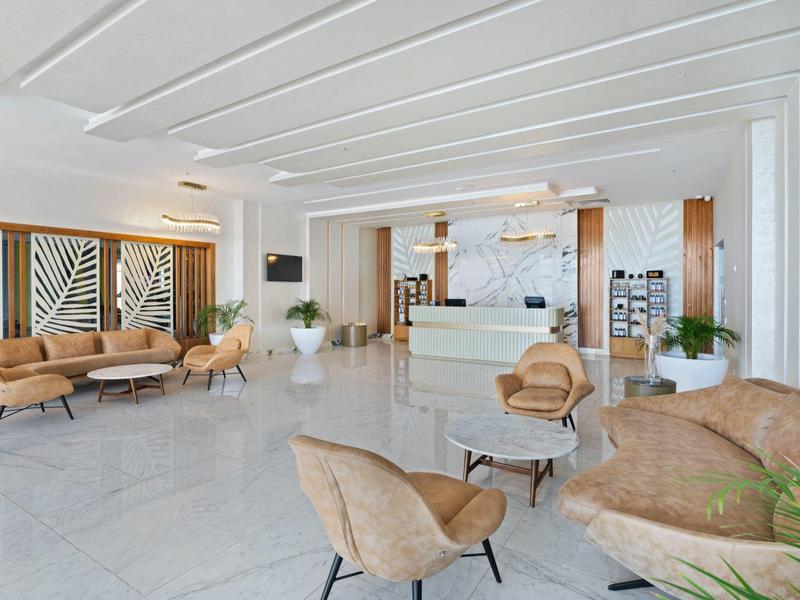 Heller, moderner Empfangsbereich mit beigen Sesseln, Sofas und kleinen Tischen auf weißem Marmorboden.