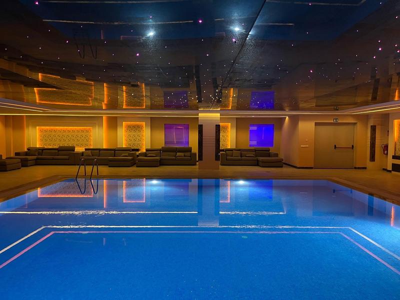 Innenraum eines Schwimmbads mit blau beleuchtetem Wasser und warmem, gelblich-orangenem Licht.