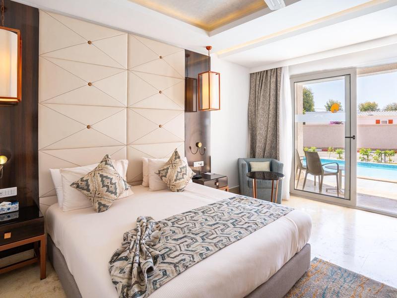 Helles Schlafzimmer mit großem Bett, gemusterten Kissen, Terrasse und Poolblick in modernem Design.