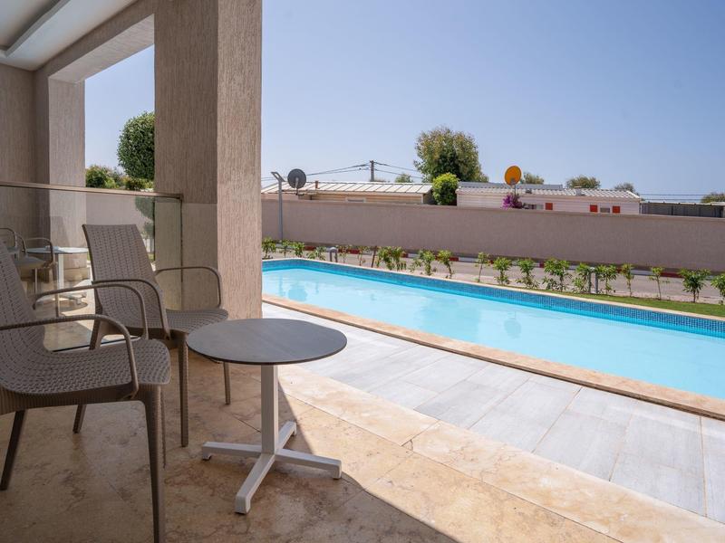 Moderner Pool mit klar blauem Wasser, umgeben von Terrasse mit Stühlen und kleinem Tisch.