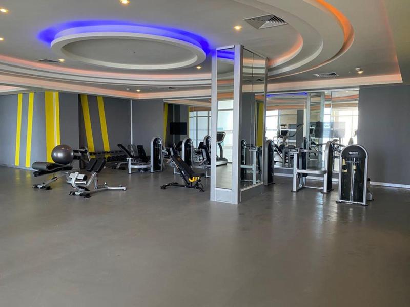 Moderner Fitnessraum mit Kraftgeräten, Spiegeln und Deckenbeleuchtung in Grau und Gelb.