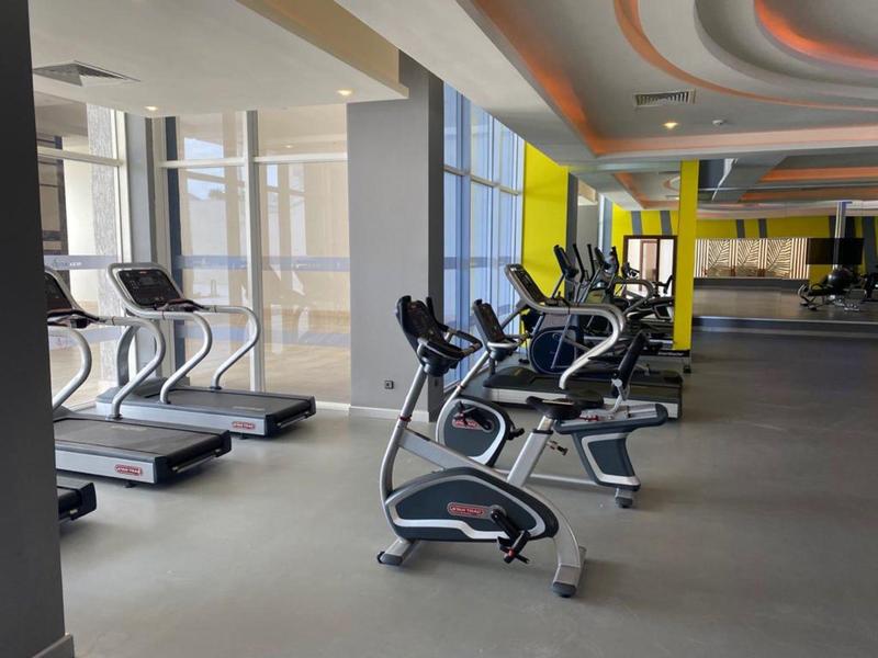 Moderner Fitnessraum mit Laufbändern und Fahrradergometern, großen Fenstern und Spiegelwand.