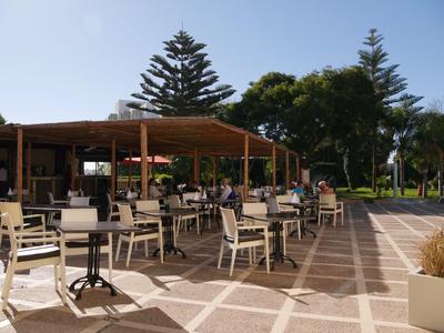 Zona de estar al aire libre con sillas y mesas frente a un hotel en un día soleado.