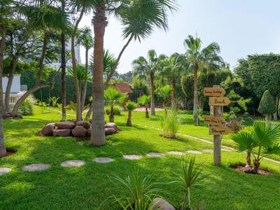 Jardín verde del hotel con palmeras, césped y señales bajo un cielo despejado.