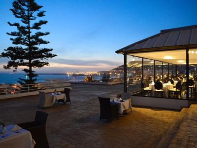 Abendliche Terrasse eines Restaurants mit Meerblick und beleuchteten Tischen in Küstennähe.