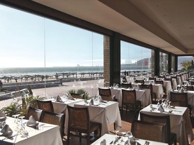 Hell eingerichtetes Restaurant mit Meerblick und gedeckten Tischen in einer Hotelanlage.