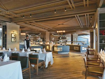 Helles Hotelrestaurant mit Holzboden, gedeckten Tischen und modernem Thekenbereich.