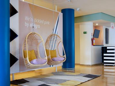 Moderne Hotellobby mit Blautönen und zwei schwebenden Korbsesseln mit lila Kissen.