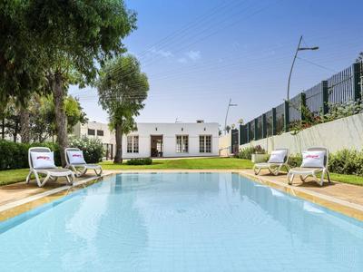 Hotelgarten mit klarem Pool, Sonnenliegen und Bäumen an einem sonnigen Tag.