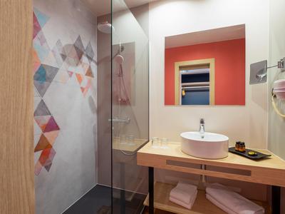 Modernes Badezimmer mit Holzwaschtisch, rundem Waschbecken und Glasdusche mit geometrischem Muster.