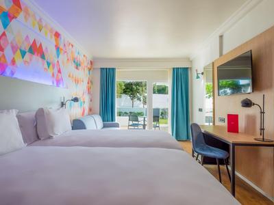 Modernes Hotelzimmer mit zwei Betten, Schreibtisch und Blick auf eine Terrasse mit Garten