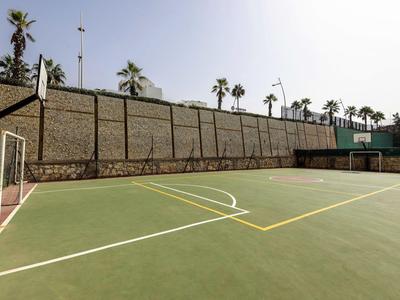 Freiluft-Sportplatz mit Tennis- und Fußballfeldern neben einer hohen Steinmauer und Palmen.