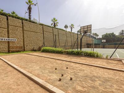 Ein Außenbereich mit einem Boule-Platz vor einer hohen Mauer und Basketballkörben.