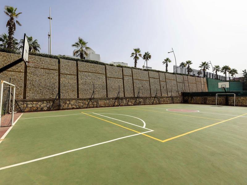 Leerer Tennis- oder Sportplatz mit Begrenzungsmauern und einigen Palmen im Hintergrund.