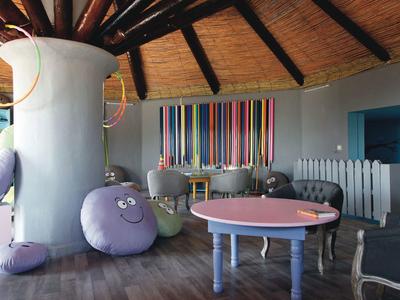 Coin de jeu et de détente coloré avec coussins ronds et tables sous un toit voûté en bois.