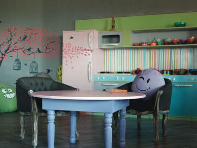 Cuisine colorée avec table bleue, deux chaises et un mur décoré d'un arbre.