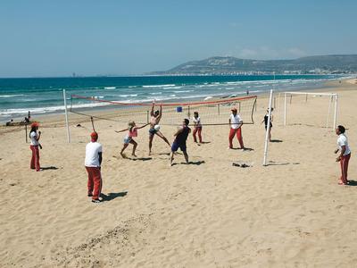 Groupe de personnes jouant au volley-ball sur la plage avec des montagnes en arrière-plan.