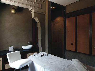 Salle de spa moderne avec table de massage, chaise et lavabo sous un éclairage doux.