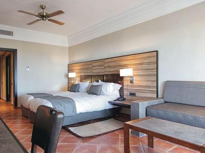 Chambre d'hôtel moderne avec lit double, canapé, tête de lit en lattes de bois et ventilateur de plafond