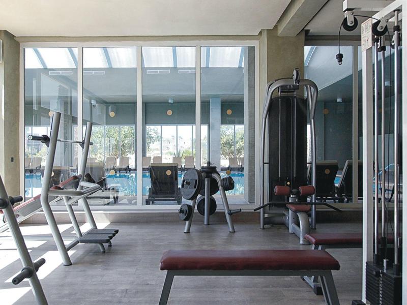 Salle de sport moderne avec équipements et grandes fenêtres vitrées donnant sur l'extérieur.