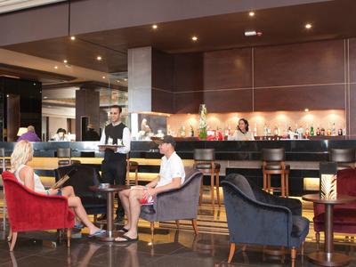 Hotelbar met gasten en ober, gezellige stoelen en gedimde verlichting.