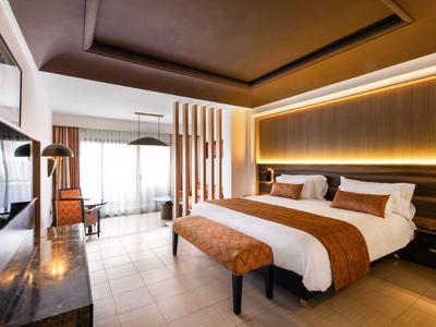 Modern hotelkamer met groot bed, tv en daglicht via grote ramen.