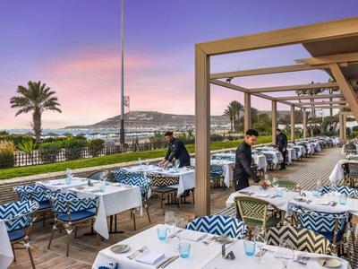 Außenrestaurant mit gedeckten Tischen und Blick auf einen Pool bei Sonnenuntergang.