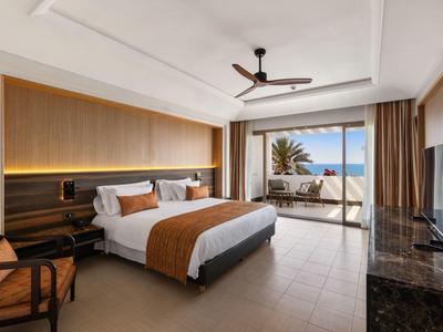 Modern hotelkamer met kingsize bed, stoel en balkon met uitzicht op zee.