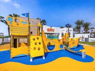 Kleurrijke speeltuin in de vorm van een schip met glijbaan en klimrekken onder een blauwe lucht.