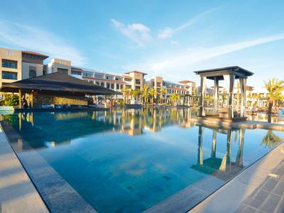 Großer Hotelpool mit Sonnenschirmen und Umgebungsgebäuden bei klarem Himmel.