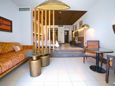 Modern ingerichte hotelkamer met bank, stoelen en decoratieve kamerverdeler.