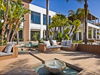 Moderner Außenbereich eines Hotels mit Sitzgruppen, Wasserbrunnen und Palmen bei sonnigem Wetter