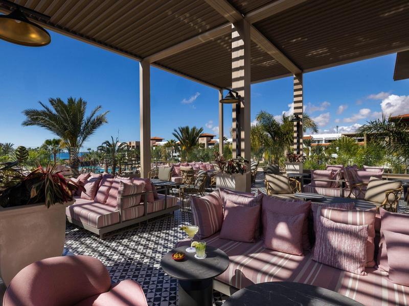 Gezellige buitenlounge met moderne meubels en uitzicht op palmbomen.