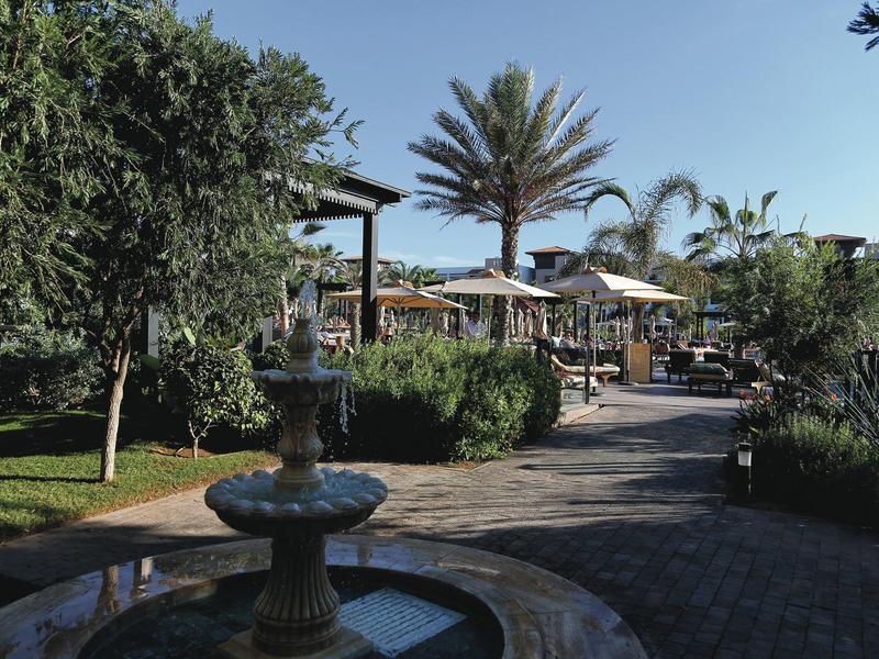 Binnenplaats met fontein, bomen en parasols bij een hotelresort.