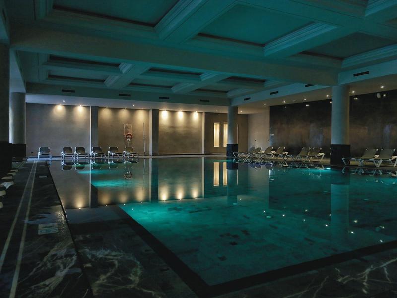 Donker binnenzwembad in een luxe spa met ligstoelen en gedempte verlichting.