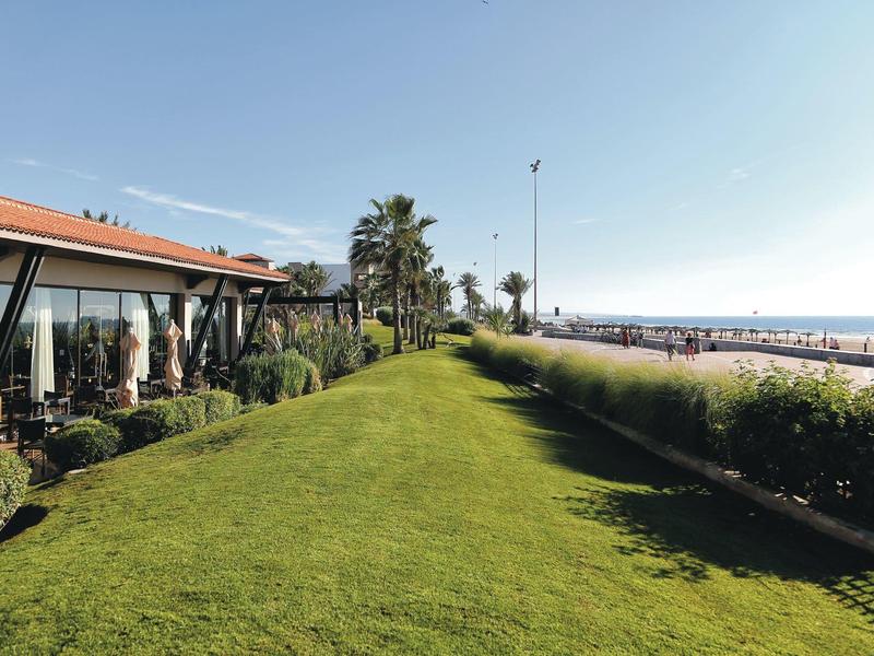 Groen gazon naast modern gebouw met uitzicht op strand en zee onder heldere lucht.
