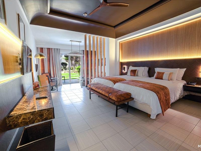 Modern hotelkamer met groot tweepersoonsbed, bankje en balkon met uitzicht op groen.