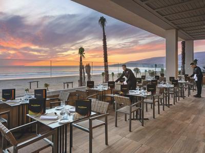 Terrasse eines Restaurants mit Meerblick bei Sonnenuntergang und gedeckten Tischen.