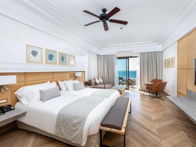 Modern eingerichtetes Hotelzimmer mit Doppelbett, Sitzecke und Meerblick vom Balkon.