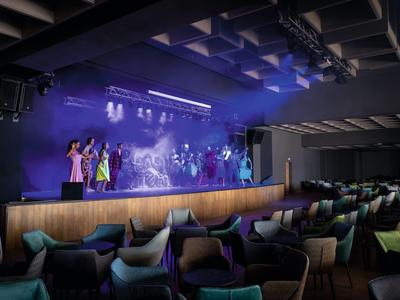 Bühne mit Schauspielern und Sitzbereich in einem Hoteltheater mit gedämpfter Beleuchtung.