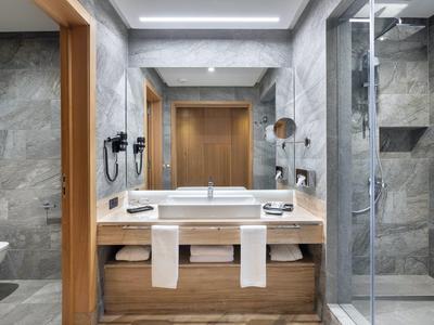 Moderne Badezimmereinrichtung mit grauen Fliesen, Doppelwaschbecken, Holzschrank und Glasdusche.