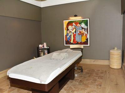 Behandlungsraum mit Massageliege, grauen Wänden, buntem Bild und Holzfußboden.