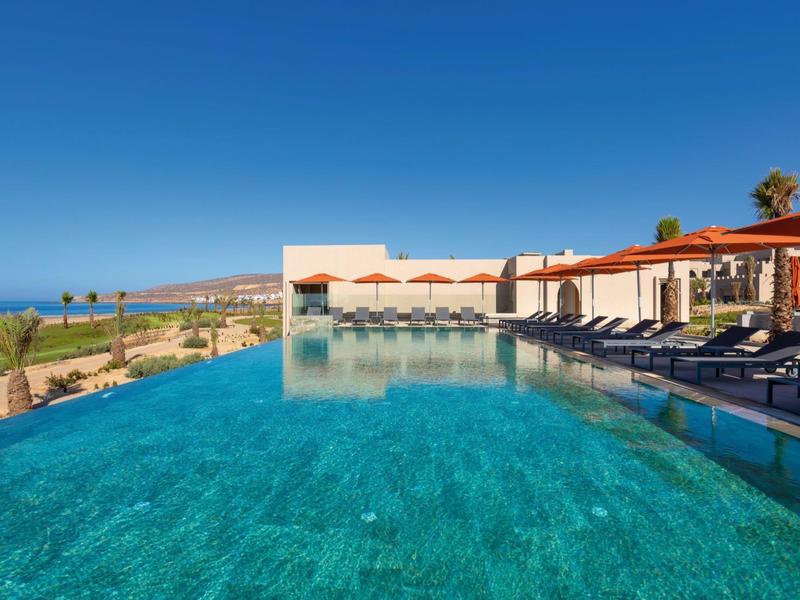 Großer Infinity-Pool mit klarem Wasser, Liegen und Blick auf Meer und Himmel bei Sonnenschein.