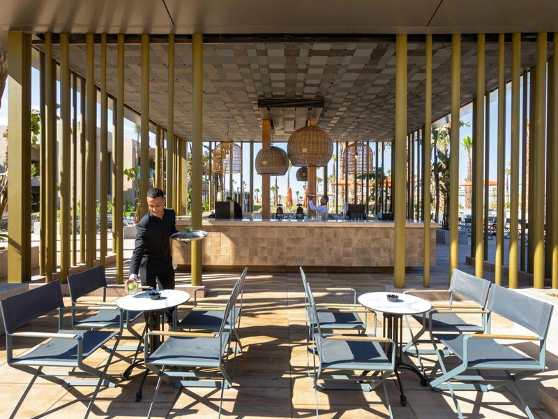 Moderner Außenbereich mit grauen Stühlen, runden Tischen und Bambusrahmen vor einer Bar.