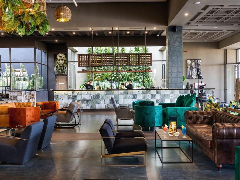 Großer, moderner Lounge-Bereich mit bunten Sesseln, Sofas, Pflanzen und Bar im Hintergrund.