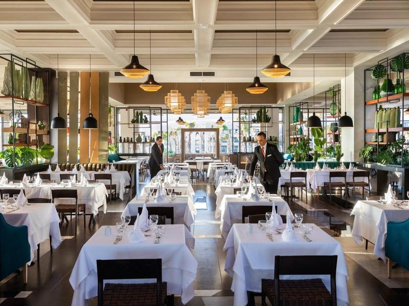 Ein helles, modern eingerichtetes Restaurant mit weißen Tischdecken, Blumen und großen Fenstern.