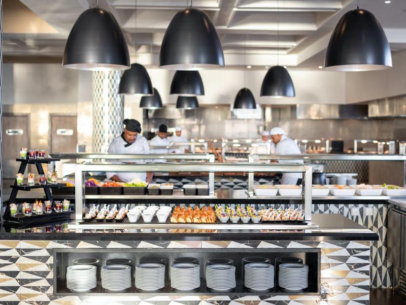 Moderne Bäckerei mit Glasvitrine, schwarzen Pendelleuchten und geometrischem Fliesenmuster.