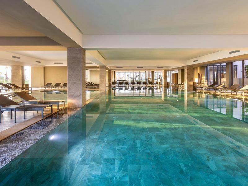 Großes Hallenbad mit türkisfarbenem Wasser, Liegestühlen und großen Fenstern für Tageslicht.