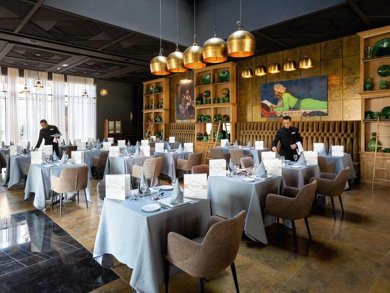 Modernes Restaurant mit elegant gedeckten Tischen, beigen Stühlen und goldenen Lampen an der Decke.