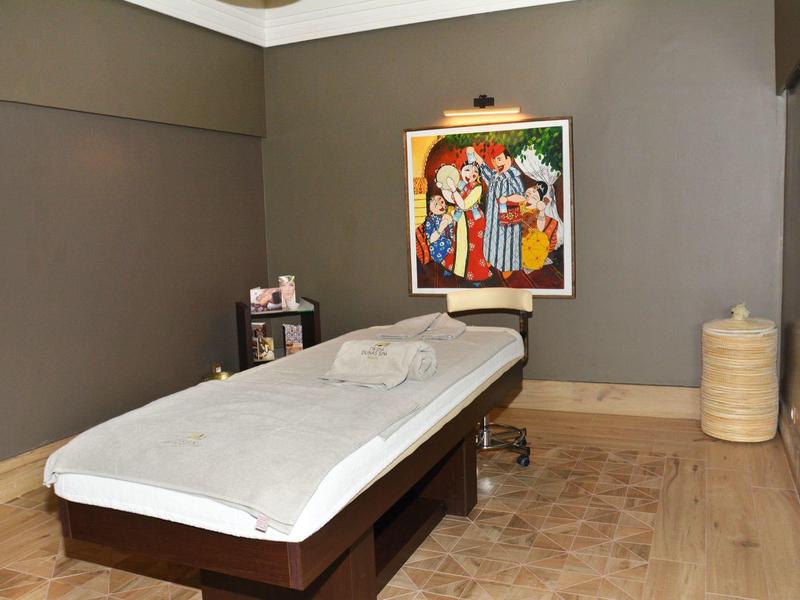 Behandlungsraum mit Massageliege, grauen Wänden, buntem Bild und Holzfußboden.